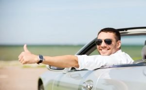 happy man driving car and showing thumbs up