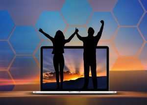 Siluette of two people standing on a laptop wtih a sunset on screen, in front of background like the image but blurred.