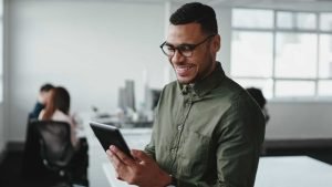 Confident smiling businessman standing in an office using a tablet